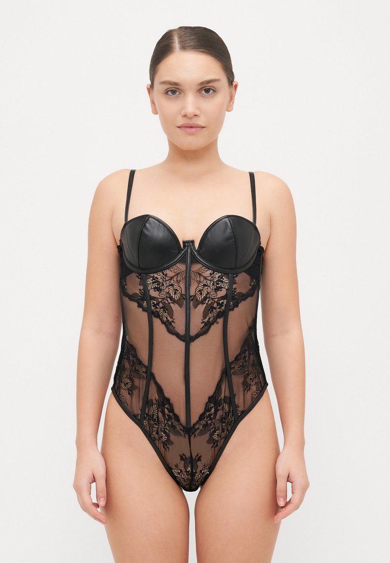 Crni bodysuit s kombinacijom kože i čipke. Kupa su oblikovana; tkanina je prozirna s cvjetnim uzorcima. Tanke naramenice i prednji zip.
