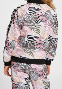 Multifarbener Trainingsanzug mit einem Blumen- und Wellenmuster in Pink, Grün, Schwarz und Orange. Hergestellt aus glattem Material mit schwarzen Akzenten.