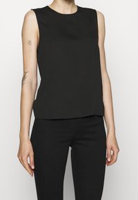 Černý bezrukávový top s kulatým výstřihem, hladkou texturou a mírně volným střihem, spárovaný s tmavými džíny. Jednoduchý a minimalistický design.