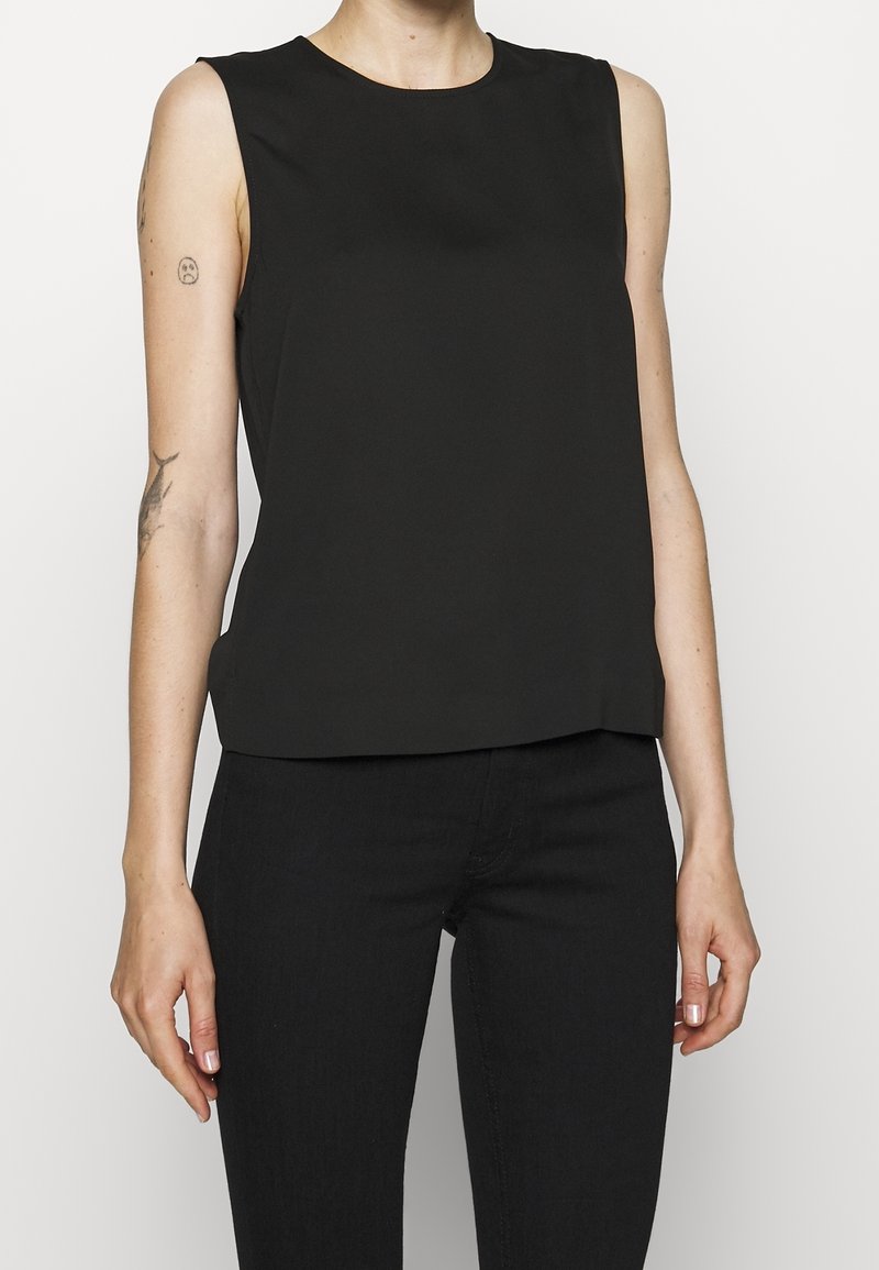 Černý bezrukávový top s kulatým výstřihem, hladkou texturou a mírně volným střihem, spárovaný s tmavými džíny. Jednoduchý a minimalistický design.