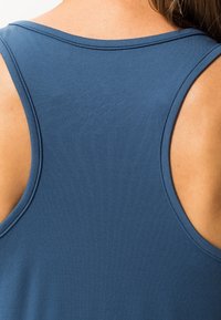 Detailní záběr na horní část zad osoby, která má na sobě modré bezramínkové tílko, zobrazující pokožku a texturu látky.
