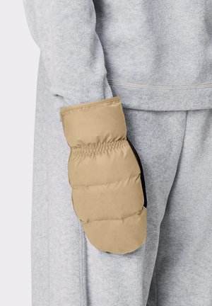 Personne portant une tenue en polaire gris clair avec une moufle rembourrée beige sur leur main, tenue le long du corps.