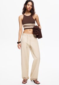 Haut en maille court marron avec des rayures beiges, associé à un pantalon large beige avec cordon de serrage. Modèle tenant un châle texturé assorti.