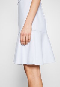 Lichtblauw flared jurk van gemusterd stof. Heeft een aansluitende lijfje en een gestructureerde hem, met een gladde en zachte oppervlakte.