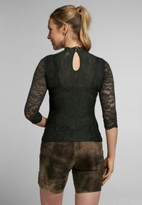 Dunkelgrünes Spitzentop mit drei Viertelärmeln, das hinten mit einem Schlüsselloch-Ausschnitt versehen ist. Kombiniert mit braunen Wildleder-Shorts.