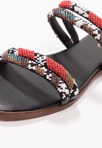 Pärl sandaler med svart läderbas. Remmarna har röda, vita, svarta, bruna och turkosa pärlor i ett mönstrat design.