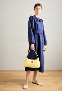 Tengerész csíkos, hosszú ruha puffos ujjakkal, összehúzott derékkal; sárga félkör alakú kézitáska fém díszítéssel; bézs lapos cipők.