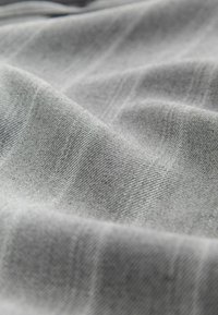 Gros plan sur un tissu gris clair doux et froissé avec une texture de tissage visible et des plis doux.