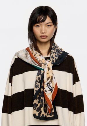 Bufanda de seda con una mezcla de patrones de leopardo y abstractos en beige, negro y naranja, colgada alrededor del cuello de un modelo.