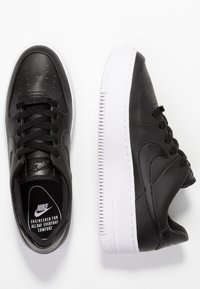 Svarta lädersneakers med vita gummisulor, med perforeringar på tåboxen och snörningen, samt en subtil Nike-logga på sidan.