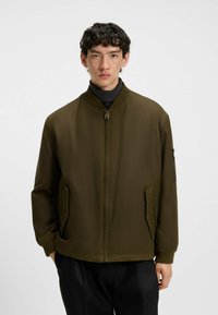 Olive green bomber jacket with a zip front, ribbed collar and cuffs, side pockets, and a zippered sleeve pocket. Features a smooth, matte finish.