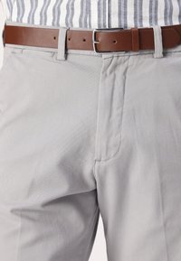 Pantalon en coton gris clair avec une ceinture en cuir marron. Comprend un devant plat, des poches et une texture lisse. Chemise rayée visible en haut.