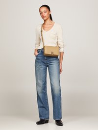 Borsa a tracolla marrone chiaro con forma rettangolare, materiale in pelle liscia e un logo prominente sul davanti. Maniche lunghe e jeans larghi, colori neutri.