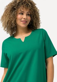 Camiseta verde de manga corta hecha de tela suave, con cuello en V y un ajuste relajado. Sencilla, de color uniforme sin patrones.