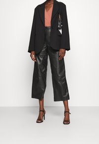 Black blazer with a structured design, paired with a dusty pink V-neck top and black leather wide-leg pants. Black strappy high heels.