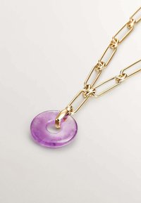 Collar de cadena de oro con un colgante circular de piedra púrpura que presenta un agujero central, mostrando una textura suave y un acabado brillante.