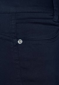 Mörkblå denimjeans med en slät yta, sidoficka med silverknappdetalj och synlig sömnad längs sömmarna.