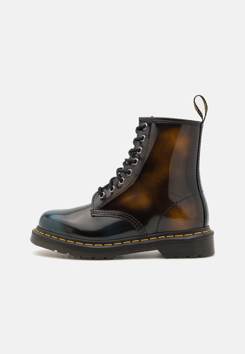 Bottine en cuir noir et marron à lacets avec surpiqûres jaunes et languette arrière sur fond blanc.