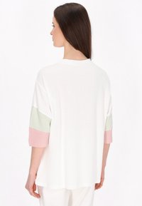 Tricou alb cu dungi, croială lejeră, cu mâneci trei sferturi în verde și roz cu modele cu dungi subțiri, decolteu rotund.