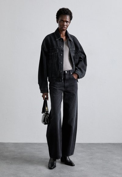 Black denim jacket over a grey top and high-waisted black jeans. The outfit is complemented by black pointed-toe boots and a small handbag.