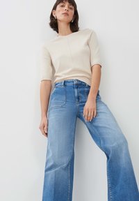 Top beige aderente con maniche corte abbinato a jeans in denim azzurri a gamba larga, caratterizzati da un'alta vita e un classico design a cinque tasche.