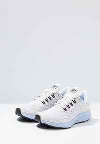 Scarpe sportive bianche con tomaia in rete testurizzata, accenti azzurri, suola nera e lacci neri. Presentano una linguetta imbottita e materiale traspirante.