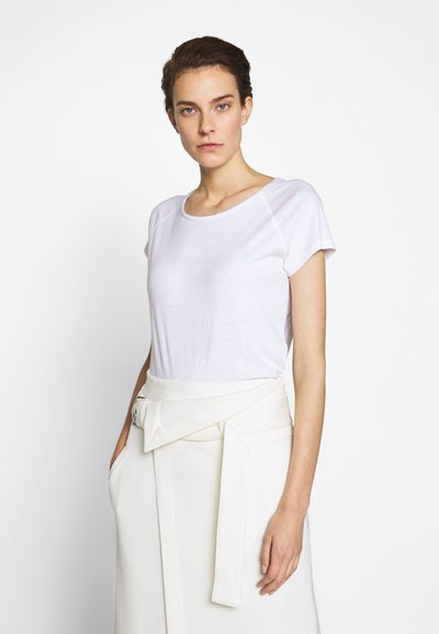 T-shirt blanc à manches courtes en tissu léger avec une coupe décontractée, associé à une jupe crème taille haute dotée d'une ceinture nouée.