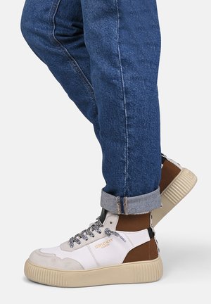 Sneakers alte con tomaia in tessuto bianco, dettagli beige e marroni, suola in gomma strutturata e lacci con motivo decorativo.