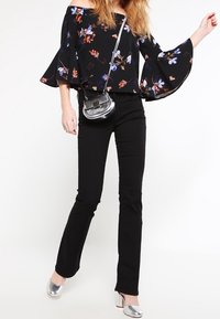 Top nero scollato sulle spalle con motivi floreali, maniche a campana, abbinato a pantaloni neri a campana e scarpe con tacco a blocco argentate.