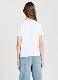 T-shirt en coton blanc à manches courtes et col rond, présentant une coupe décontractée. Assorti à un jean en denim bleu clair.