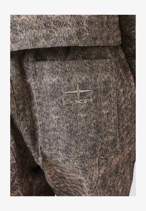 Brauner strukturierter Stoff mit einem marmorierten Muster, ausgestattet mit einer Gesäßtasche und einem gestickten Logo in einer helleren Farbe.