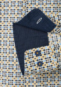 Hemdsärmel mit zwei marineblauen Knöpfen, nach hinten umgeschlagen, um das einfarbige dunkelblaue Innenfutter zu zeigen, das mit blauen, braunen, schwarzen und gelben Quadraten gemustert ist.