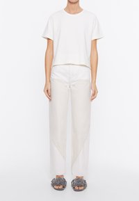 T-shirt bianco a maniche corte con collo rotondo, abbinato a pantaloni larghi beige chiaro con dettagli di cuciture diagonali. Sandali con zeppa grigi a fiori.