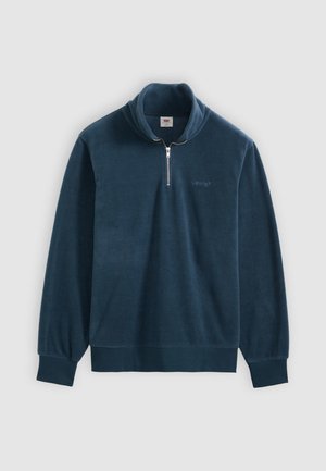 Tamsiai mėlynas fliso megztinis su ketvirtine užtrauktuko apykakle, ribinėmis rankogaliais ir apačia. Ant krūtinės yra mažas logotipas, lygus paviršius.