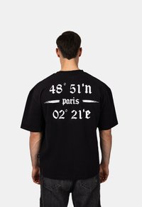 Černé bavlněné tričko s kr átkým rukávem, na zadní straně s bílým potiskem: "48° 51’n paříž 02° 21’e". Standardní střih, volný design.