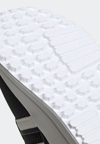 Svart sula av sneakers med en texturerad vit gummiyta, med ett hexagonalt mönster och räfflade sektioner för grepp.