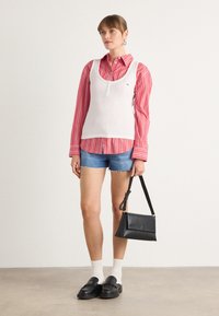 Hvit ribbestrikket tanktop over en rødstripet skjorte med knapper, kombinert med denimshorts. Svart veske, svarte platå sko og hvite sokker.