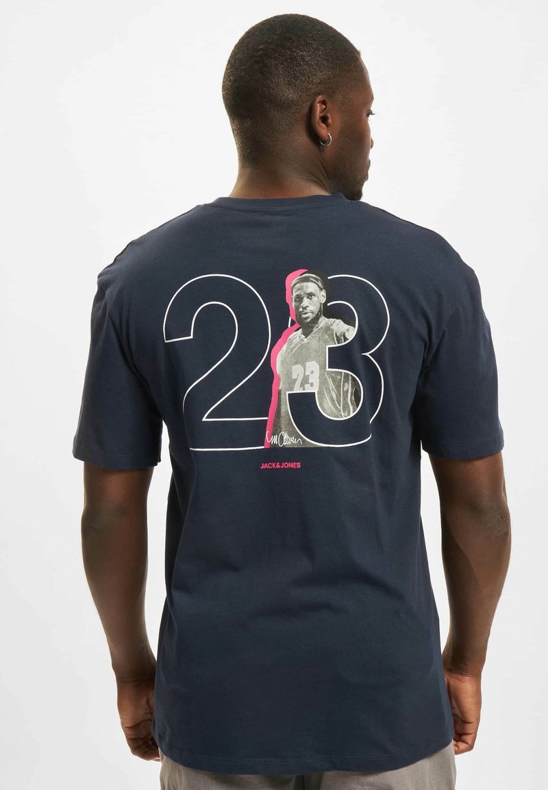 Mørkeblå bomulls T-skjorte med et stort hvitt "23" med rosa aksent, og en trykt svart-hvitt grafikk av en idrettsutøver på baksiden.