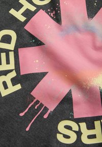 Sort stof med et stort rosa stjernedesign og gul tekst. Designet inkluderer sprøjtaccents i pastel farver.