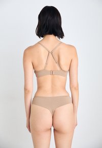 Podprsenka a bikiny v světle béžovém materiálu s nastavitelnými ramínky, křížovým střihem na zádech a bezešvým střihem spodního dílu. Hladká textura.