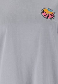 T-Shirt mit kleinem, farbenfrohem Bergmotiv und dem Text "Atme die frische Luft, beobachte die Schönheit der Natur" auf der oberen Brust.