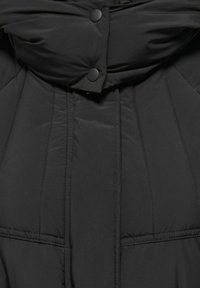 Must puffer-jakk, millel on kõrge krae, klopsklõpsuga sulgur ning peen tikand vertikaalsete õmblustega ja kaks esist taskut.