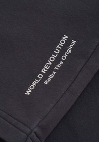 T-shirt en coton gris foncé avec le texte imprimé "RÉVOLUTION MONDIALE" et "Relux L'Original" en blanc, présentant un design simple et une texture douce.