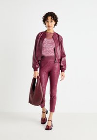 Veste bomber en cuir bordeaux, haut léger avec motif script, leggings ajustés en imprimé léopard, sac à main assorti et chaussures Mary Jane en cuir verni.