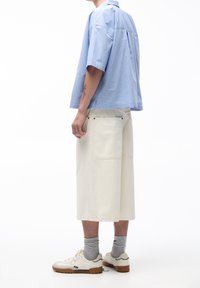 Koszula z krótkim rękawem w niebieskie paski o luźnym kroju, zestawiona z białymi szortami sięgającymi do kolan, które mają dwie tylne kieszenie i widoczne szwy.