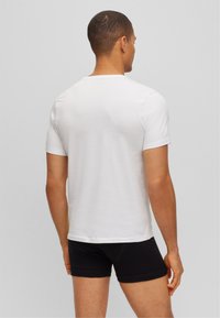 T-shirt blanc à manches courtes en coton doux. Design simple avec un col rond, vu de dos, associé à un short noir.
