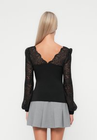 Black top with long, lace sleeves and a deep V-back. The bodice is fitted, while the sleeves feature intricate lace patterns. Gray pleated skirt.
