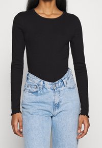Schwarzer langärmliger Bodysuit mit Rundhalsausschnitt, kontrastiert durch hellblaue hochtaillierte Jeans aus Denim mit Knopf- und Taschendetails.