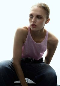 Top de tirantes rosa con purpurina, hecho de un material brillante, combinado con unos vaqueros de mezclilla azul oscuro. Modelo posando sentada, con una expresión concentrada.