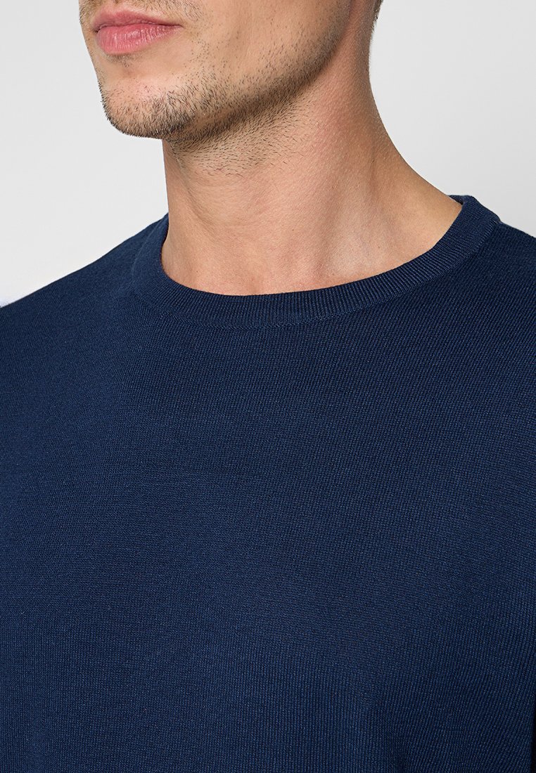 Maglione lavorato a maglia blu navy con scollatura a girocollo, caratterizzato da una superficie testurizzata e polsini a coste. Vista ravvicinata che mostra i dettagli del tessuto.